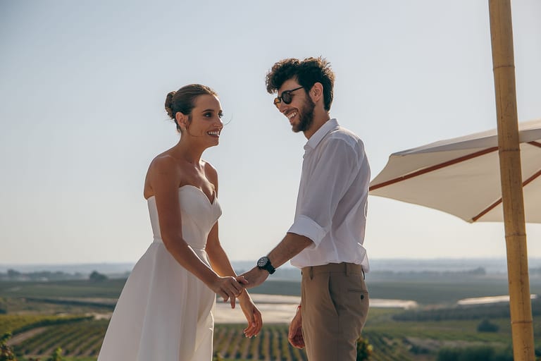 הכלה והחתן אוחזים ידיים וצוחקים מתחת לשמשייה
