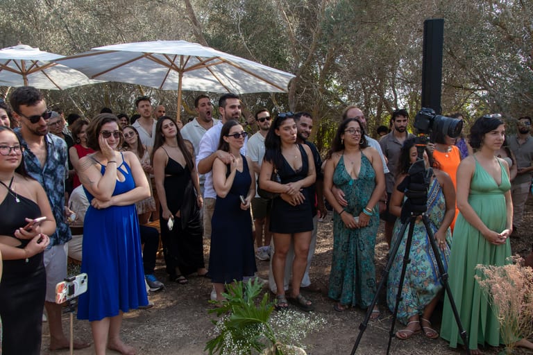 אורחים עומדים וצופים, מצלמת וידאו על חצובה