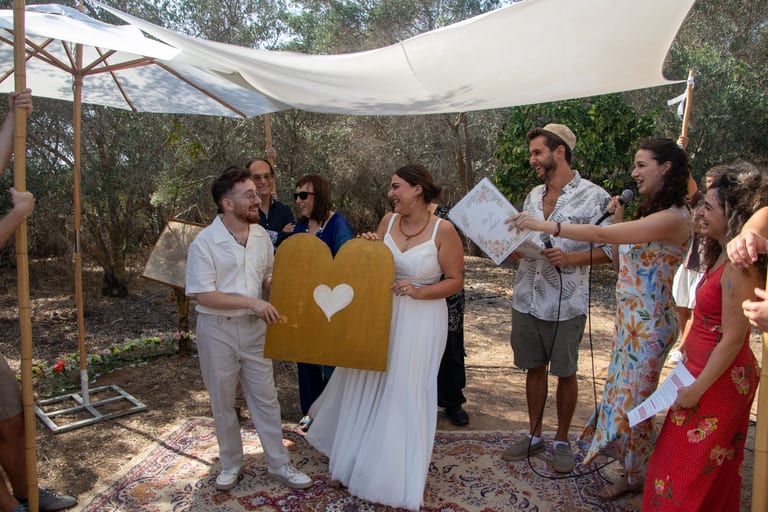 הכלה והחתן מחזיקים שלט זהב בצורת לב בזמן שאורחים נואמים