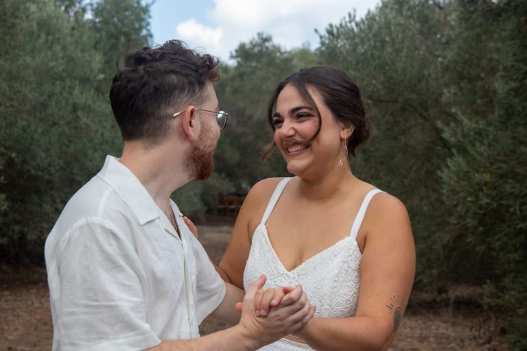 הכלה והחתן אוחזים ידיים ומביטים זה בזה בצחוק