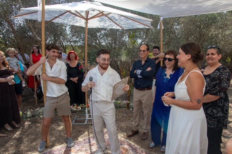 הכלה והחתן עומדים עם בני משפחה מתחת לשמשיות