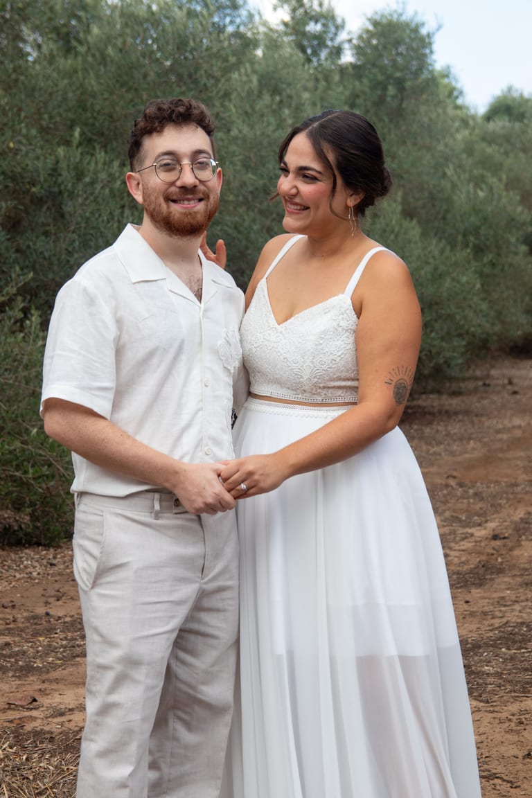 הכלה והחתן עומדים יד ביד ומחייכים זה לזה