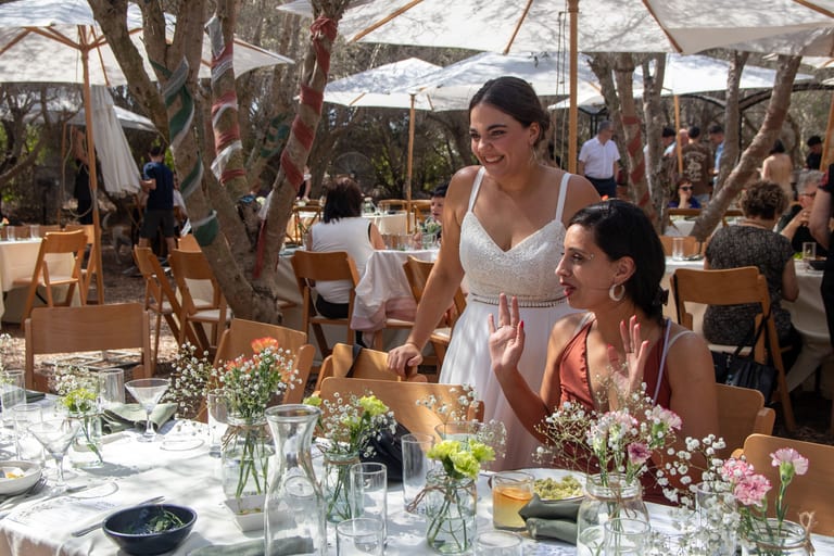 הכלה צוחקת עם אורחת ליד שולחן ערוך עם פרחים
