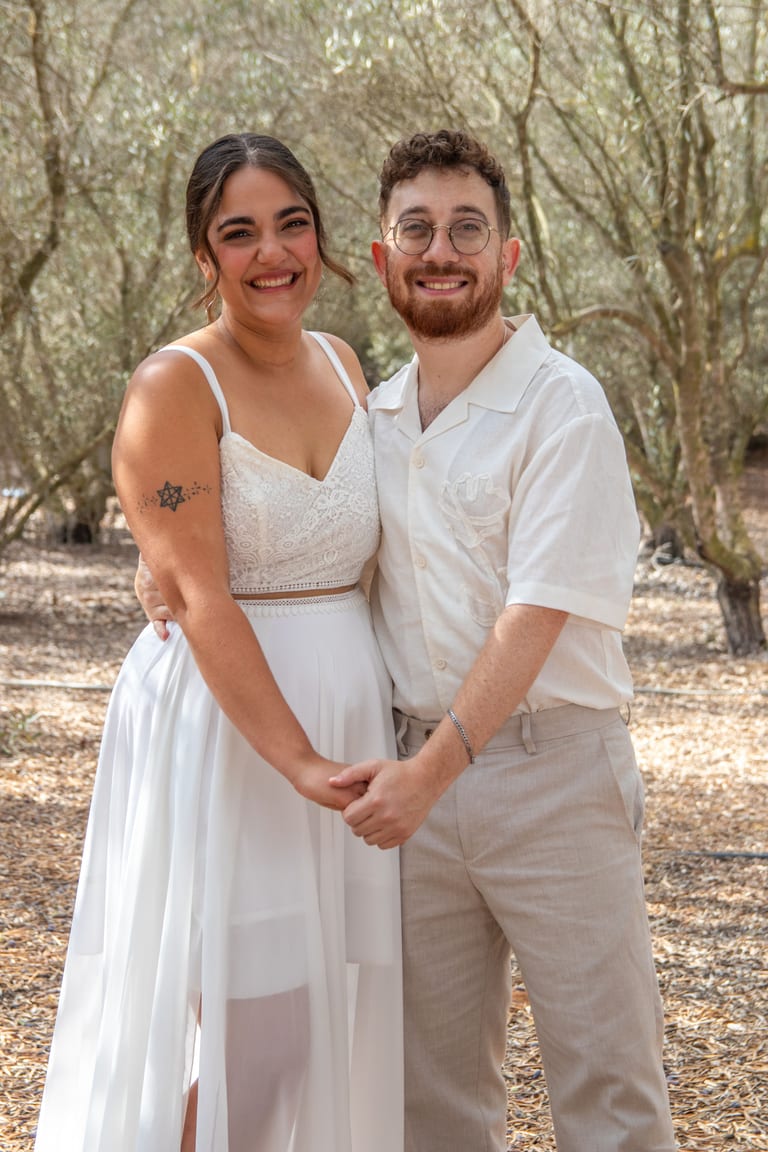 הכלה והחתן מצטלמים אוחזים ידיים ומחייכים